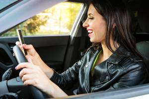 woman holding steering wheel looking at phone