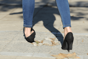 woman in heels hurting her ankle on a cracked sidewalk
