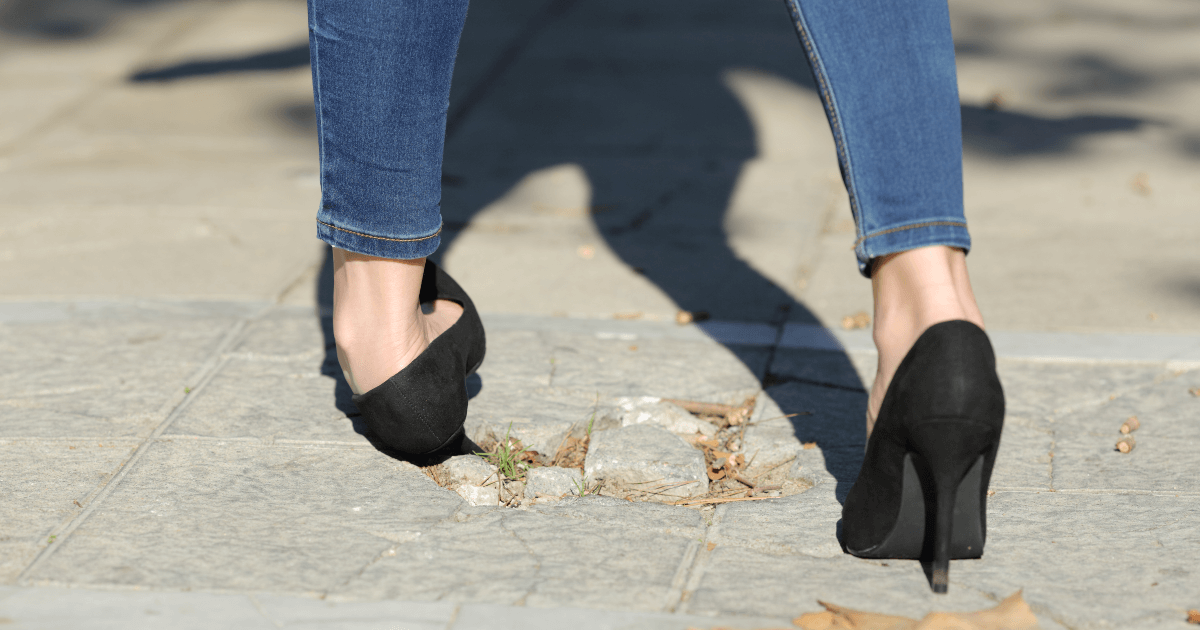 woman in heels hurting her ankle on a cracked sidewalk