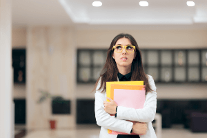 A nervous-looking woman walking through an office holding paperwork.