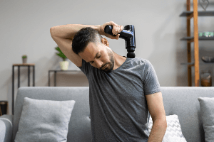 Man using massage gun on his own shoulder.