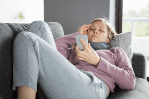 Sick woman lying on a couch using her cell phone.