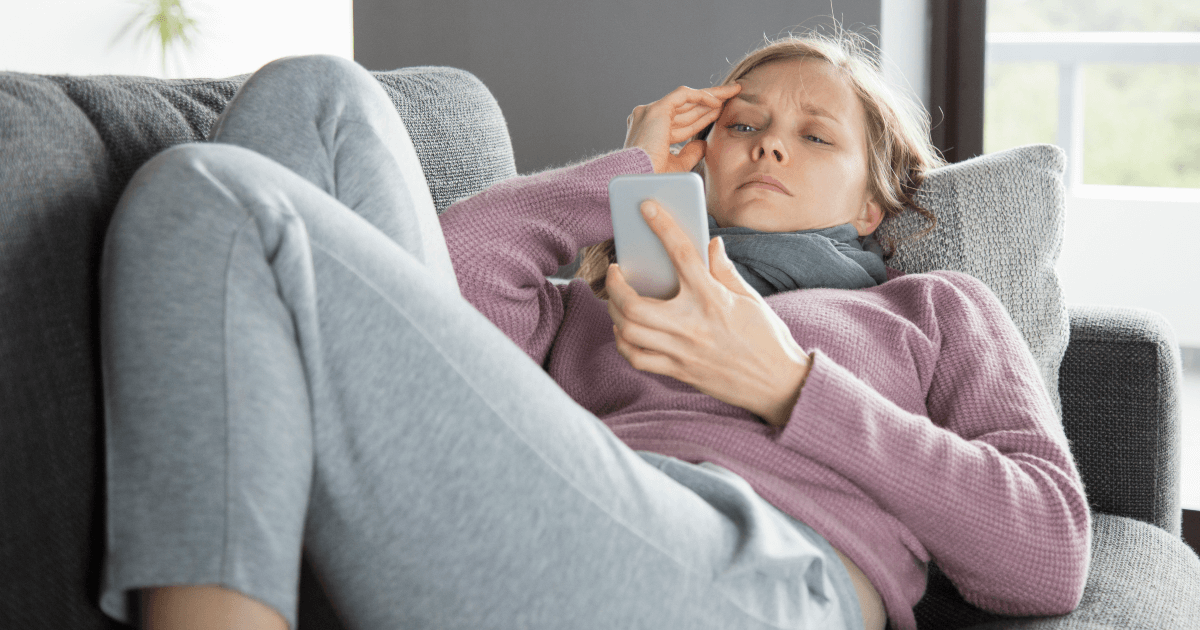 Sick woman lying on a couch using her cell phone.