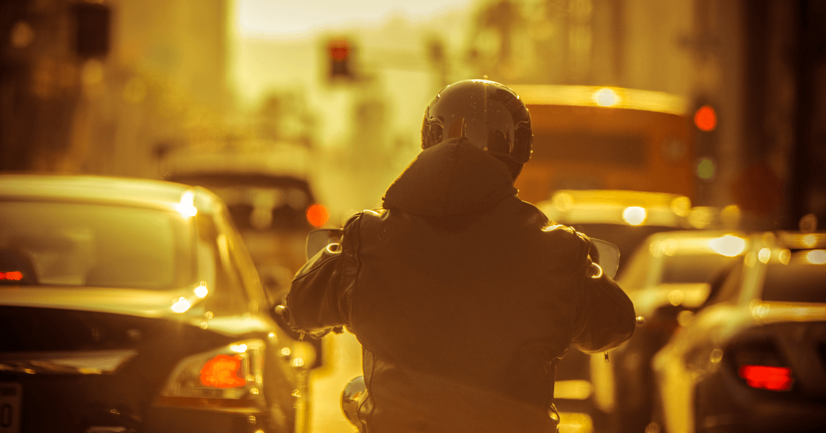 Motorcyclist driving through heavy traffic while the sun sets.