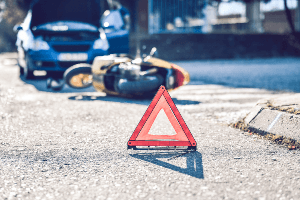 Road hazard sign in front of mangled motorcycle with a vehicle behind it. 