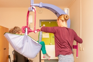 caregiver using a Hoyer lift to move a young patient