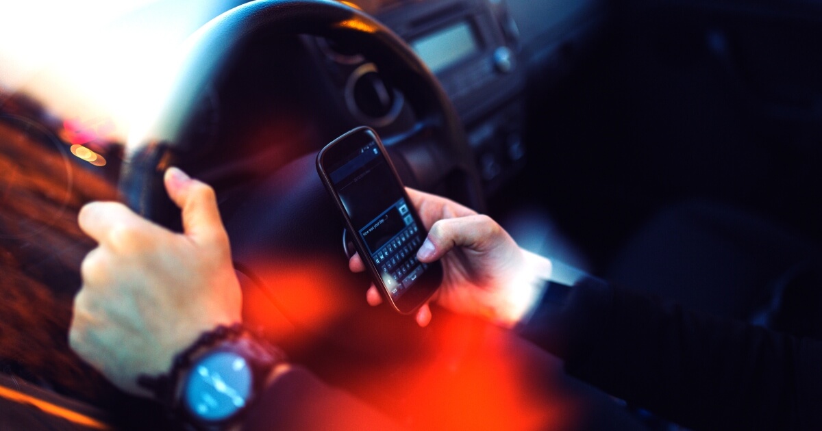 photo illus shows hands of a driver texting