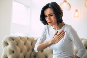young woman at home clutching her chest in pain