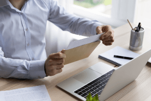 man opening a letter in front of his computer